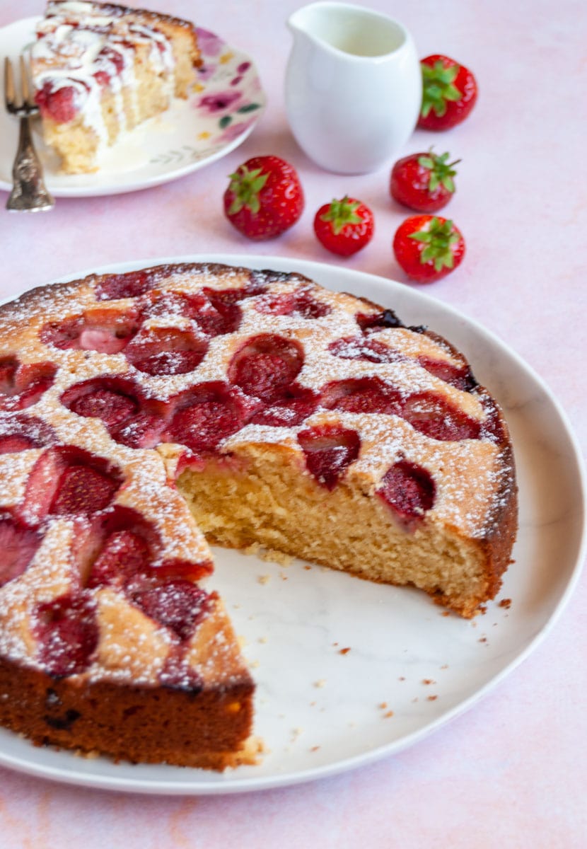 A round strawberry cake with a slice cut out on a white plate.