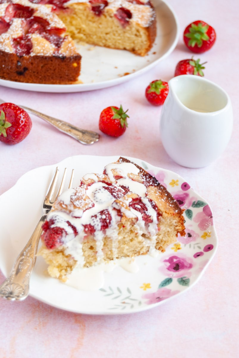 a slice of strawberry cake drizzled with cream on a floral plate with a silver cake fork.