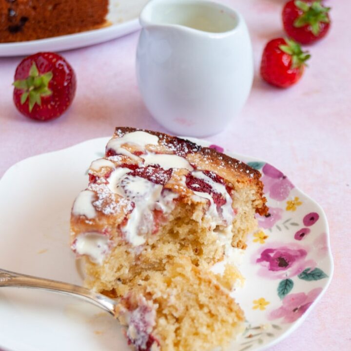 a slice of strawberry cake drizzled with cream with a silver fork on a floral plate.