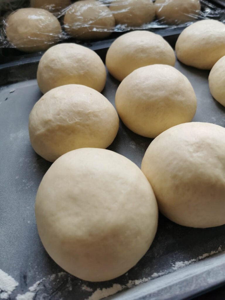 unbaked doughnuts proving on a silver baking tray