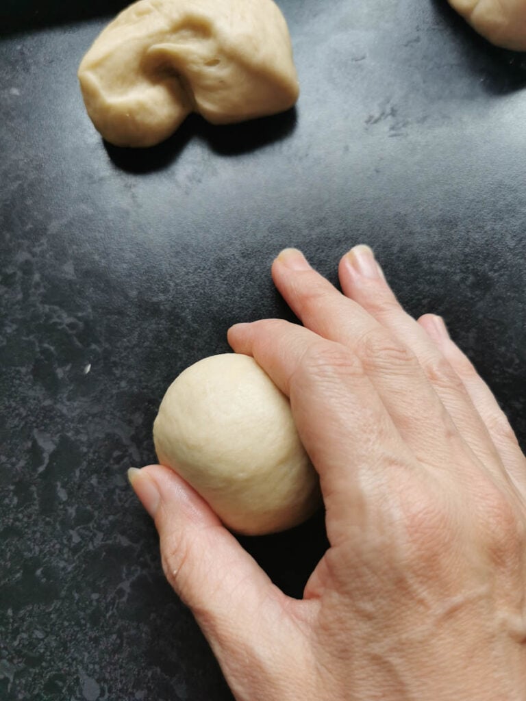 a hand rolling a piece of dough on a grey work surface
