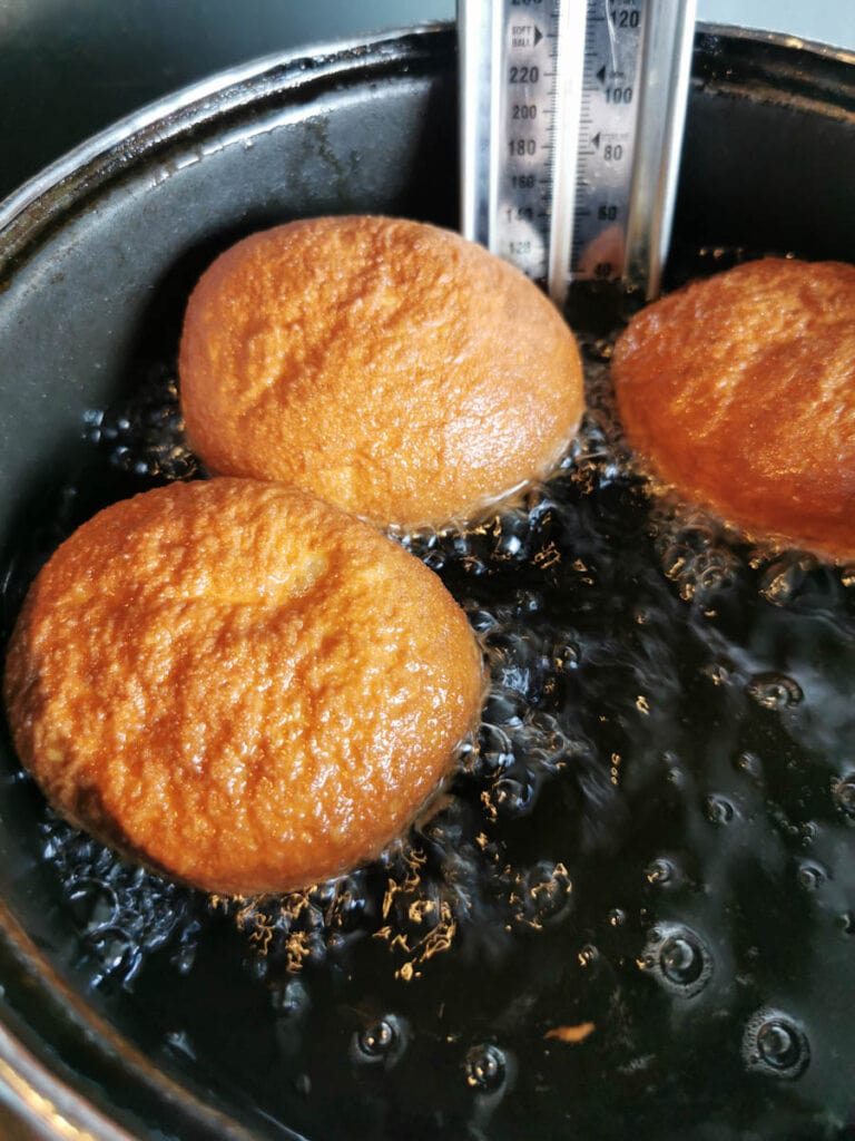 three doughnuts frying in a large saucepan