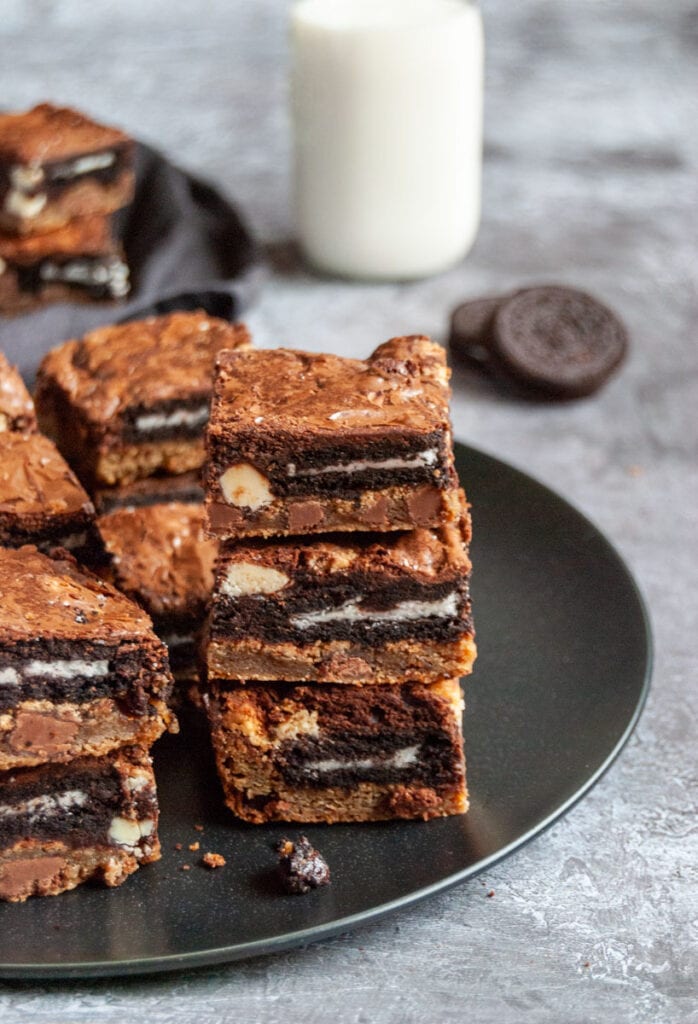 cookie dough brownies stuffed with Oreo cookies on a black plate with a glass bottle of milk in the background.