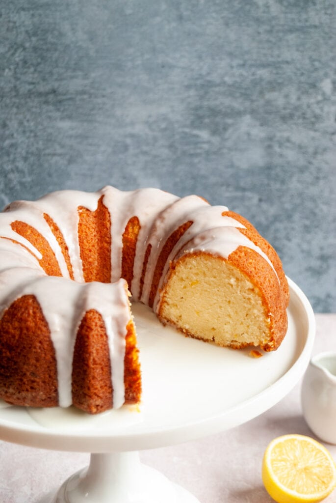 a sliced lemon bundt cake with white lemon icing on a white cake stand.