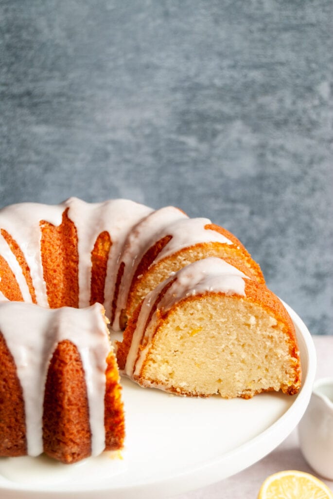 a sliced lemon bundt cake with white icing on a white cake stand.