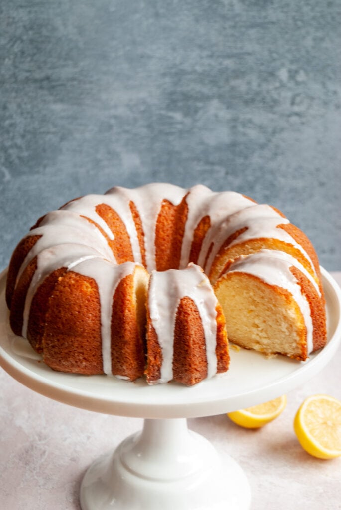 a lemon bundt cake covered in white icing on a white cake stand.