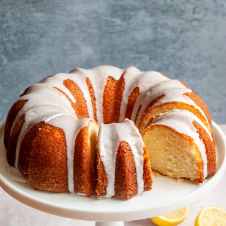 a lemon bundt cake covered in white icing on a white cake stand.