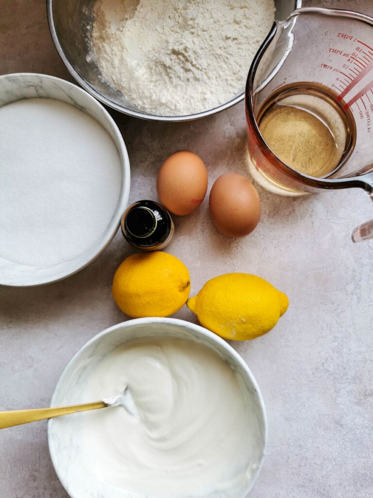 bowls of sour cream, sugar, flour, two lemons, two eggs and a jug of oil.