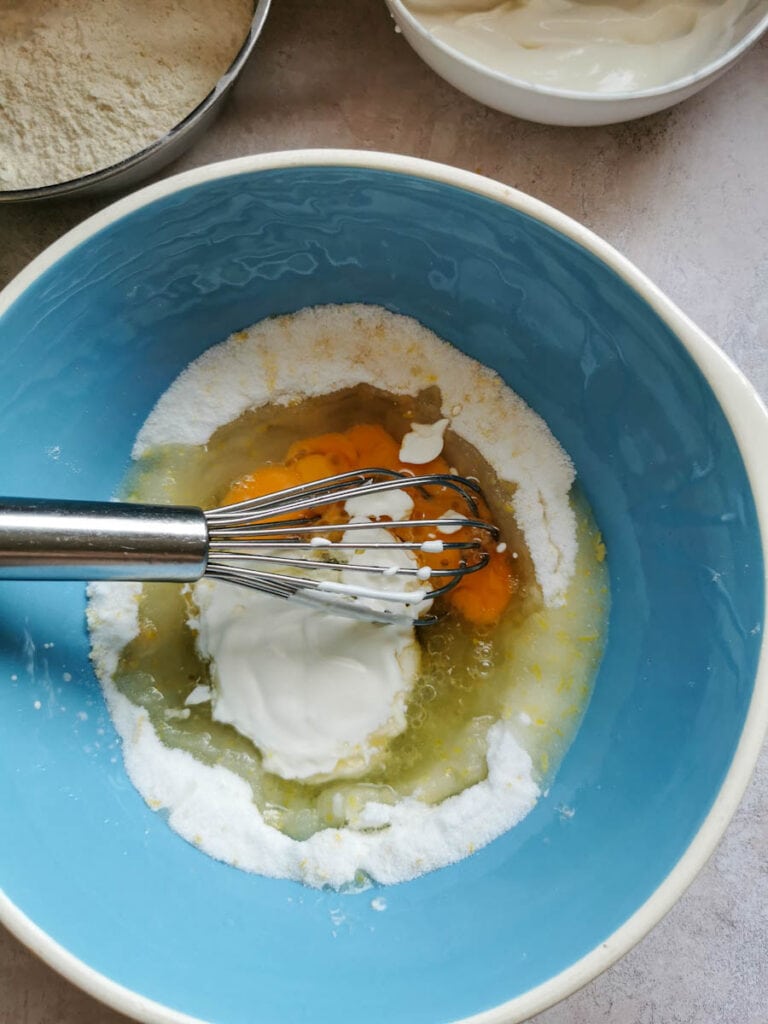 a blue and white bowl of sour cream, eggs, sugar and flour being whisked to make a cake batter