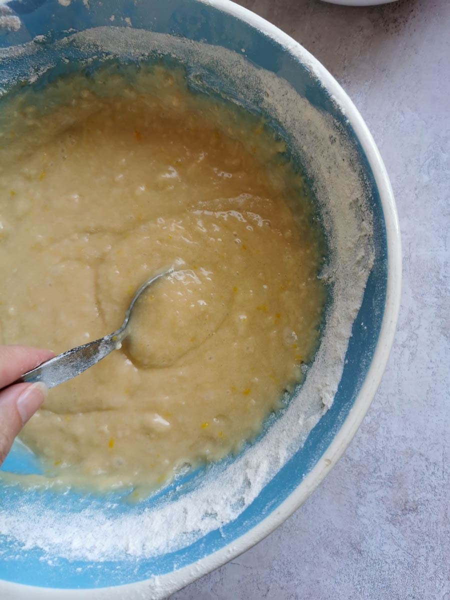flour being folded into a bowl of cake mixture with a silver spoon.