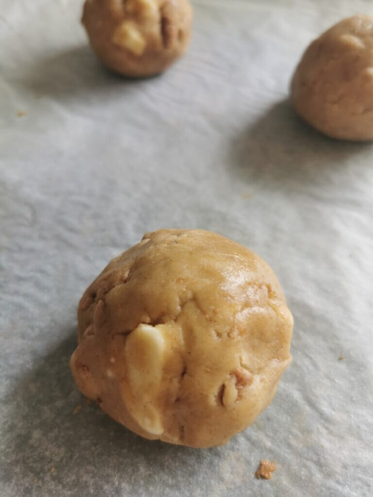 Biscoff and white chocolate cookie dough balls on a lined baking sheet