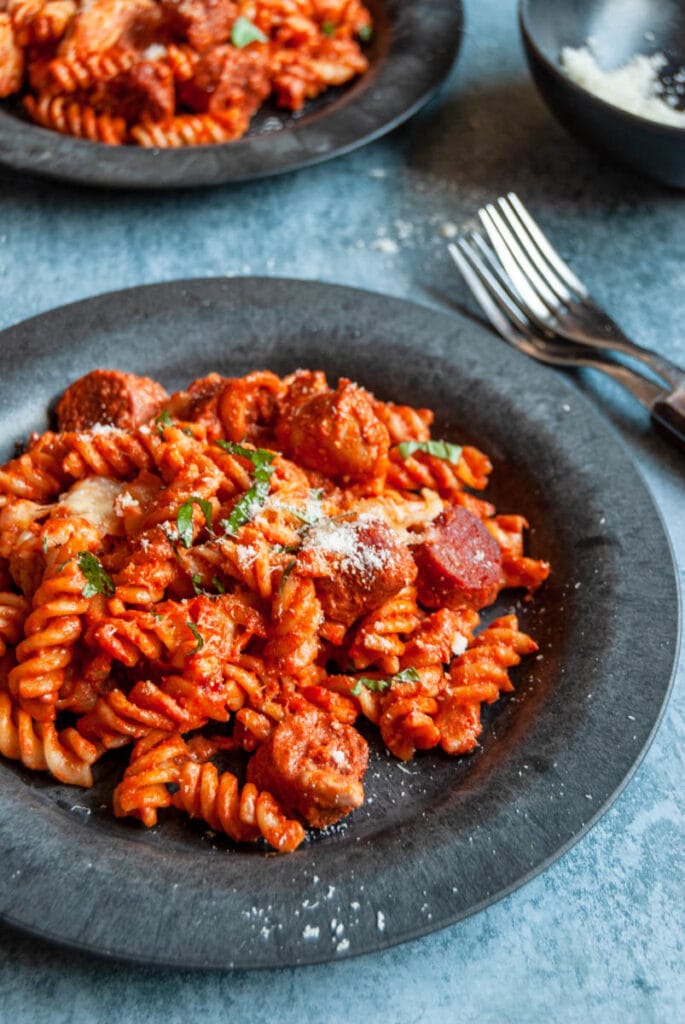 a plate of pasta with chicken and chorizo in a tomato sauce sprinkled with pamesan cheese. 