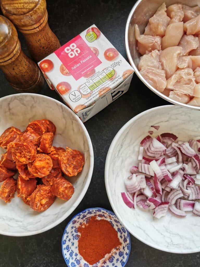 Bowls of diced chicken, chorizo sausage, sliced red onion, a carton of tomato passata, a pot of smoked paprika and wooden salt and pepper mills