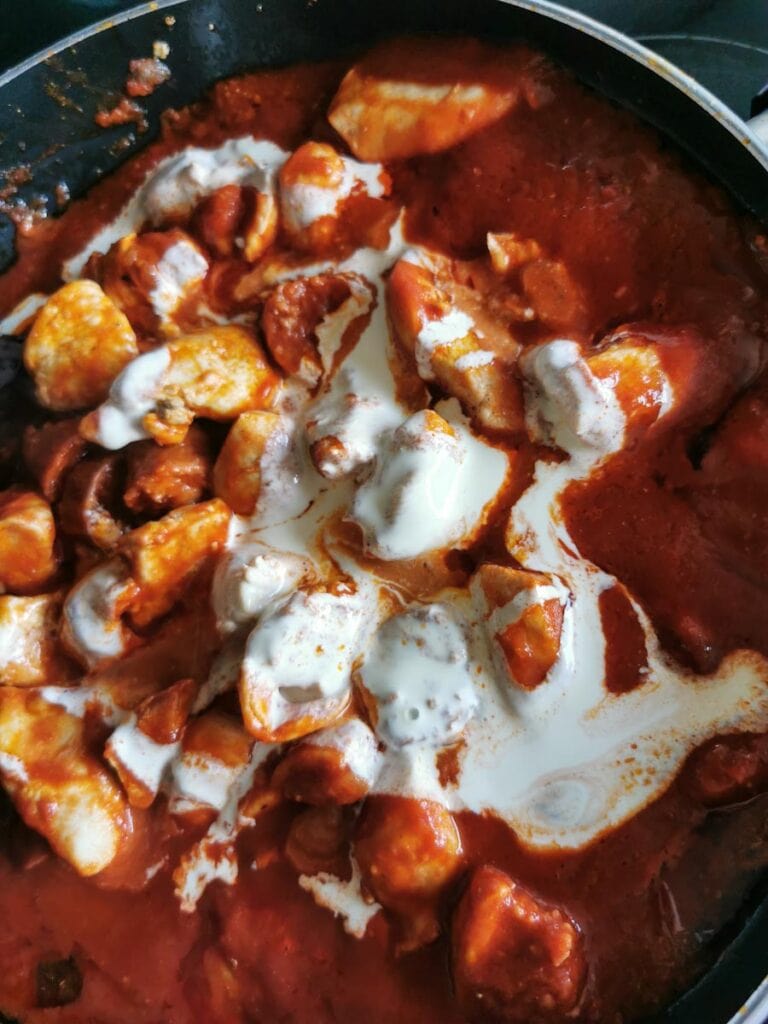 A creamy tomato pasta sauce with chicken chunks and chorizo sausage in a frying pan.