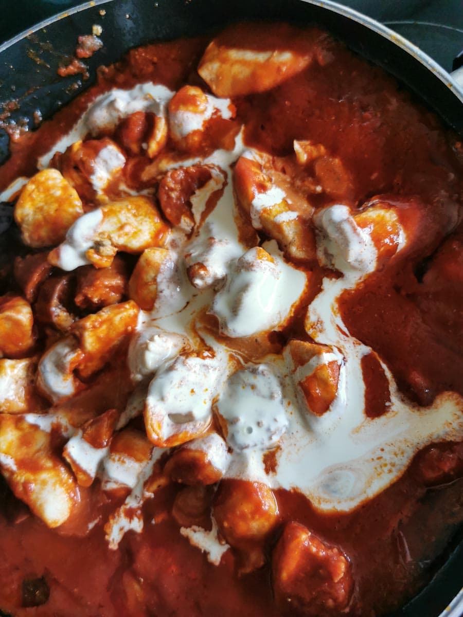 A creamy tomato pasta sauce with chicken chunks and chorizo sausage in a frying pan.