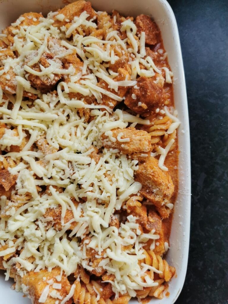 Tomato pasta with chicken chunks and chorizo sausage sprinkled with cheese in a white casserole dish.