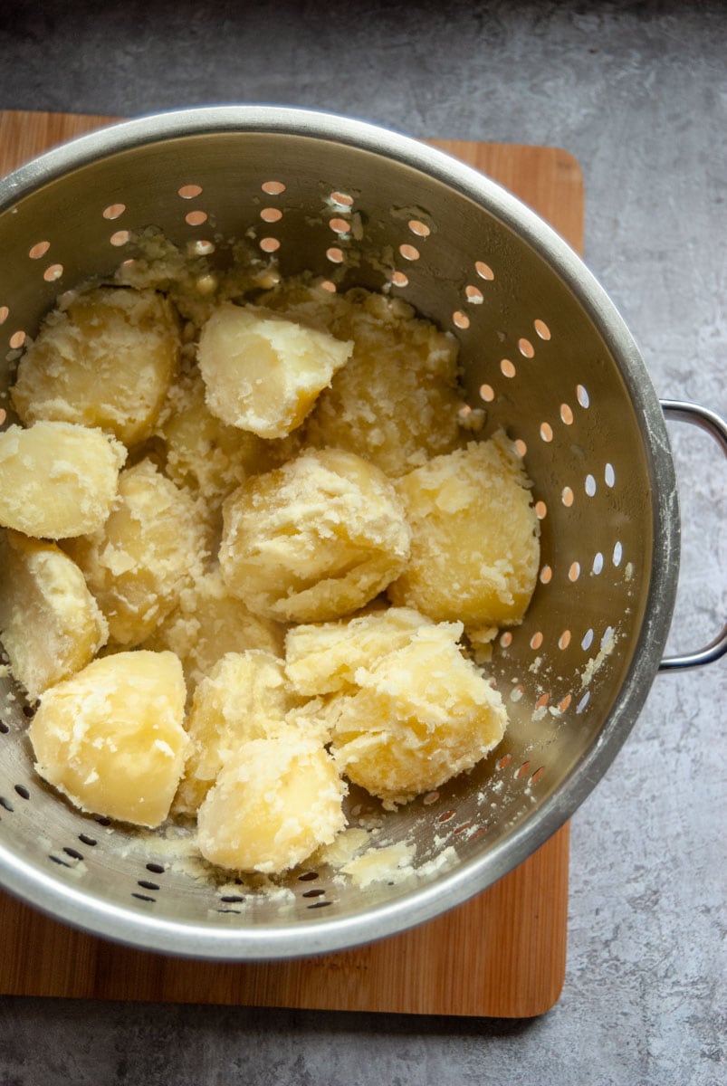 a colander of freshly boiled potatoes on a wooden chopping board.