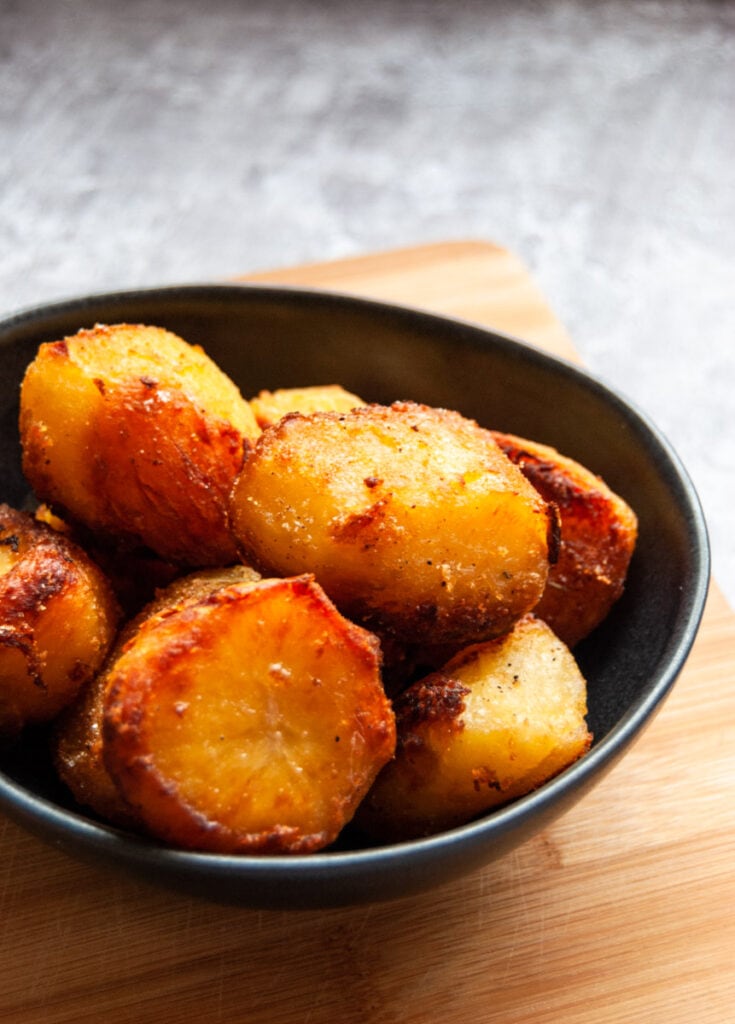 a small black bowl filled with roasted potatoes on a wooden chopping board.