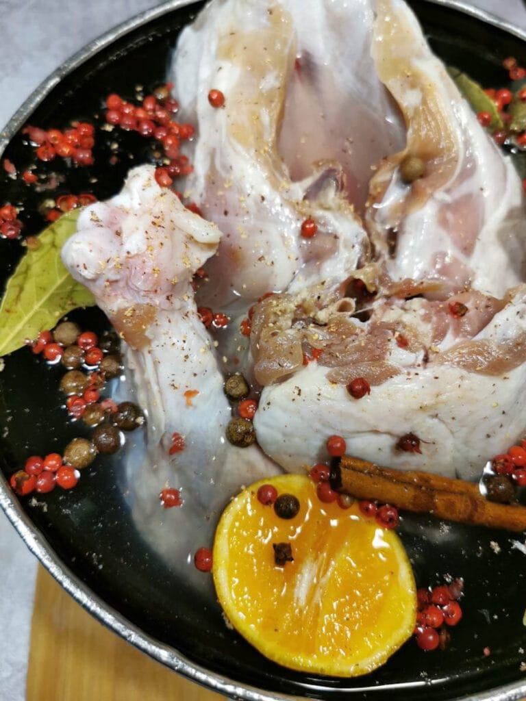 a turkey crown soaking in a brine solution with cinnamon sticks, orange slices and spices.
