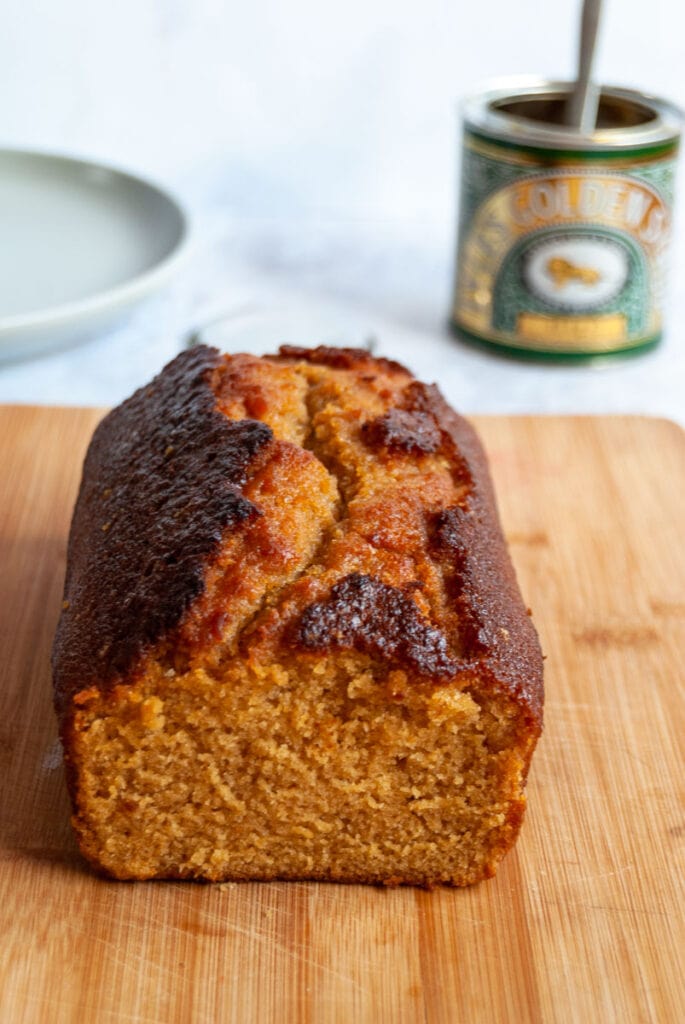 a golden syrup loaf cake on a wooden board with a tin of golden syrup in the background.