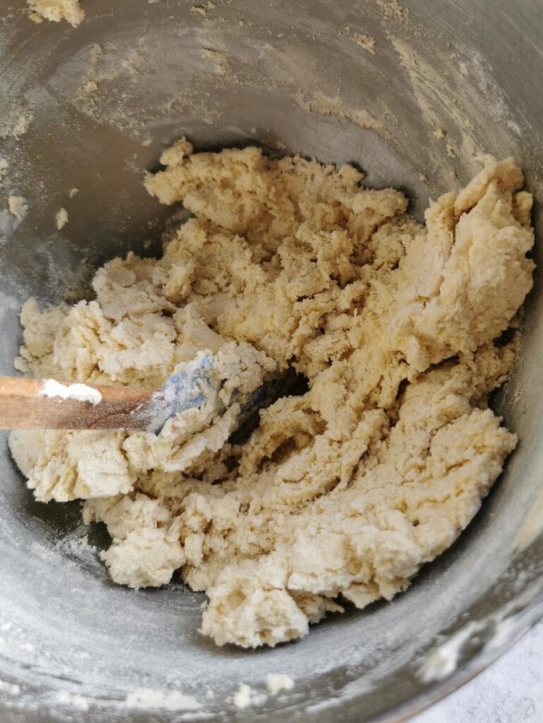 Unbaked biscuit dough in a silver mixing bowl with a wooden spatula.