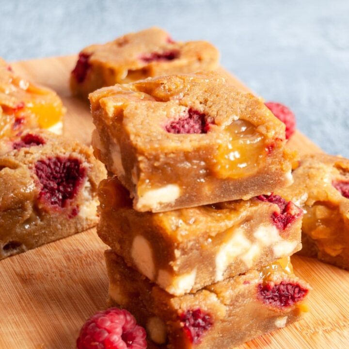 three blondie bars with raspberries, lemon curd and white chocolate chunks on a wooden board.