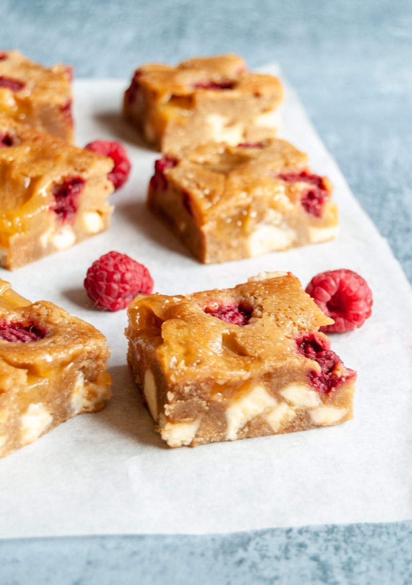 lemon raspberry blondie bars with white chocolate chunks on a piece of baking paper with fresh raspberries