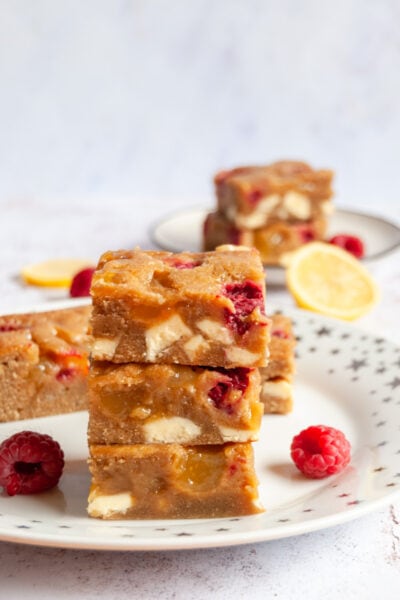 three lemon blondie bars with raspberries and white chocolate chunks on a gold star plate.