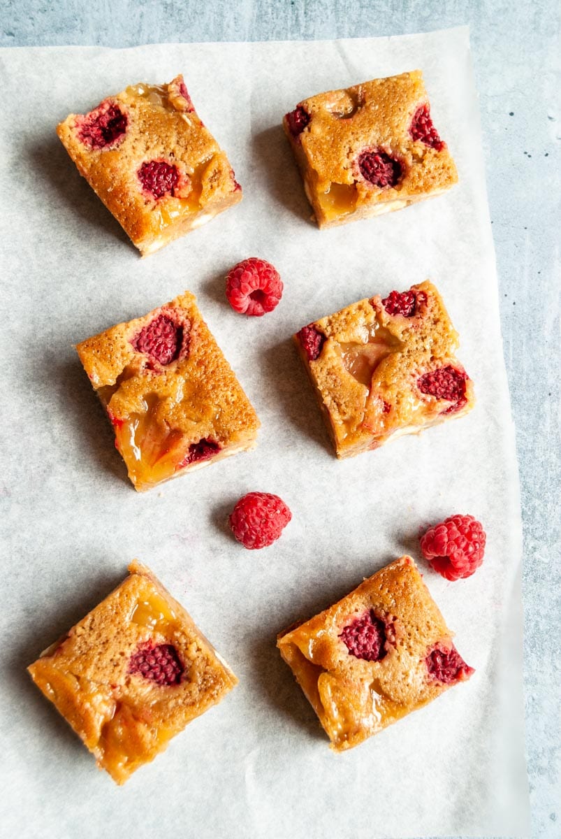 six lemon blondie with white chocolate chunks and raspberries on a piece of baking paper.