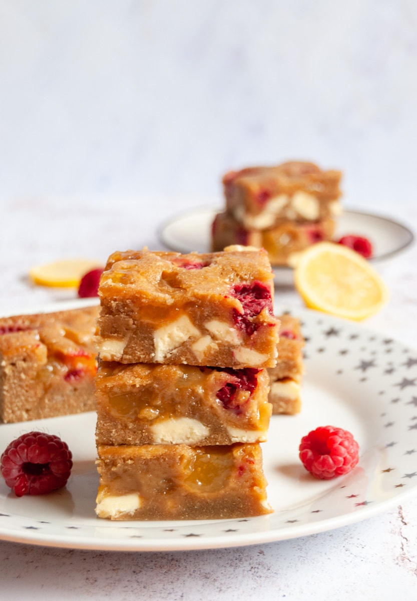 three lemon blondie bars with raspberries and white chocolate chunks on a gold star plate.
