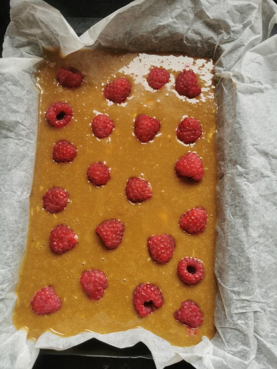 blondie batter with fresh raspberries poured into a lined baking tin
