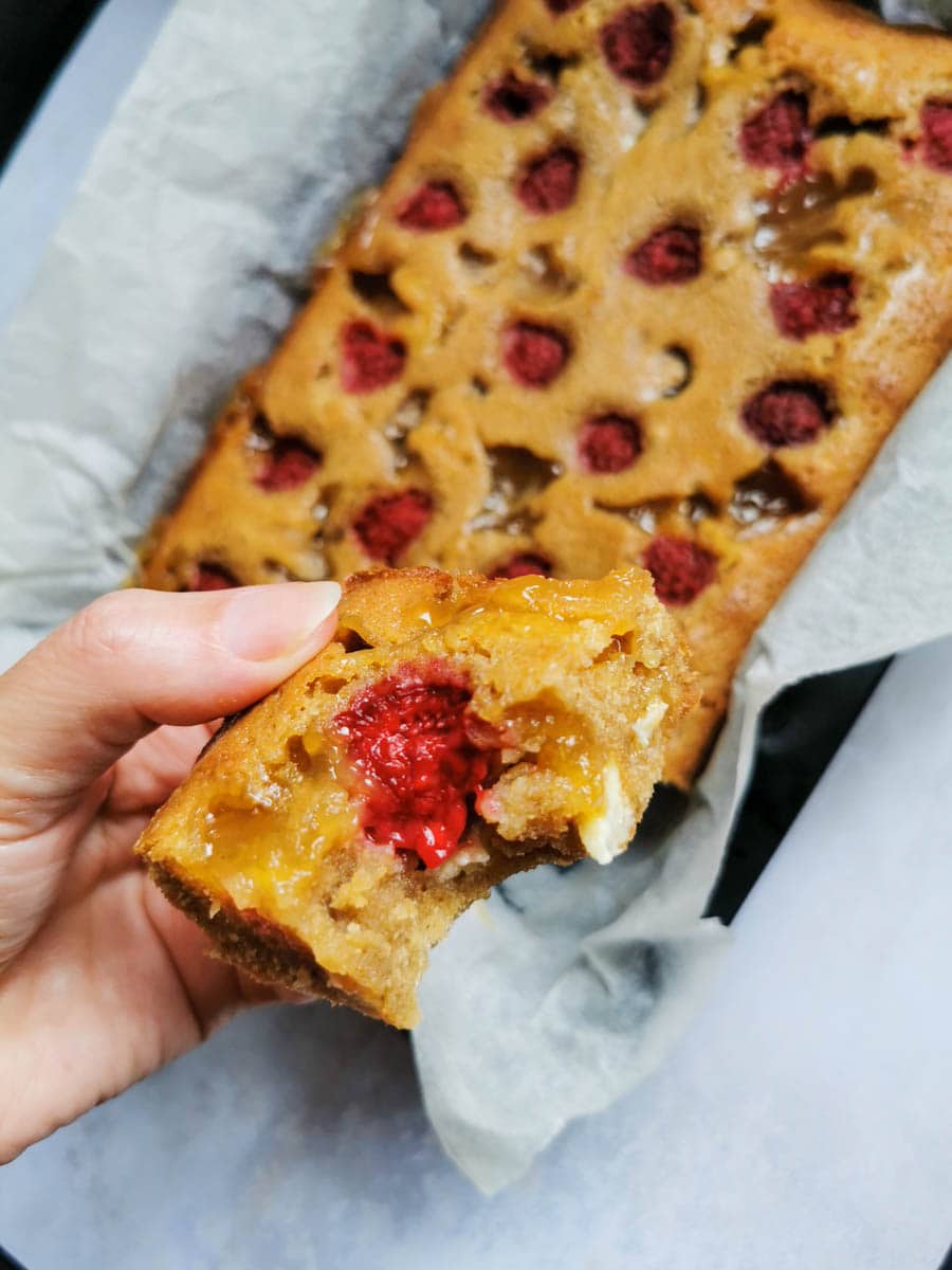 A hand holding a lemon and raspberry blondie with a tray of the blondies in the background