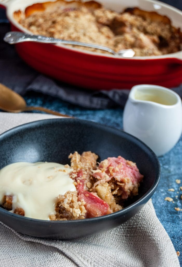 a bowl of rhubarb crumble with custard and a small white jug of custard.