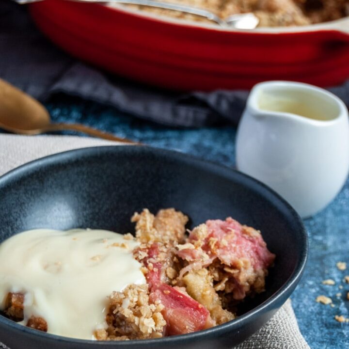 a bowl of rhubarb crumble with custard and a small white jug of custard.