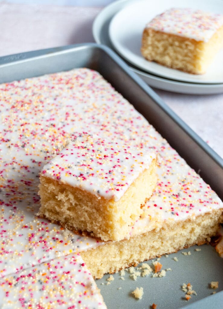 a vanilla sponge traybake cake covered in white icing and sprinkles