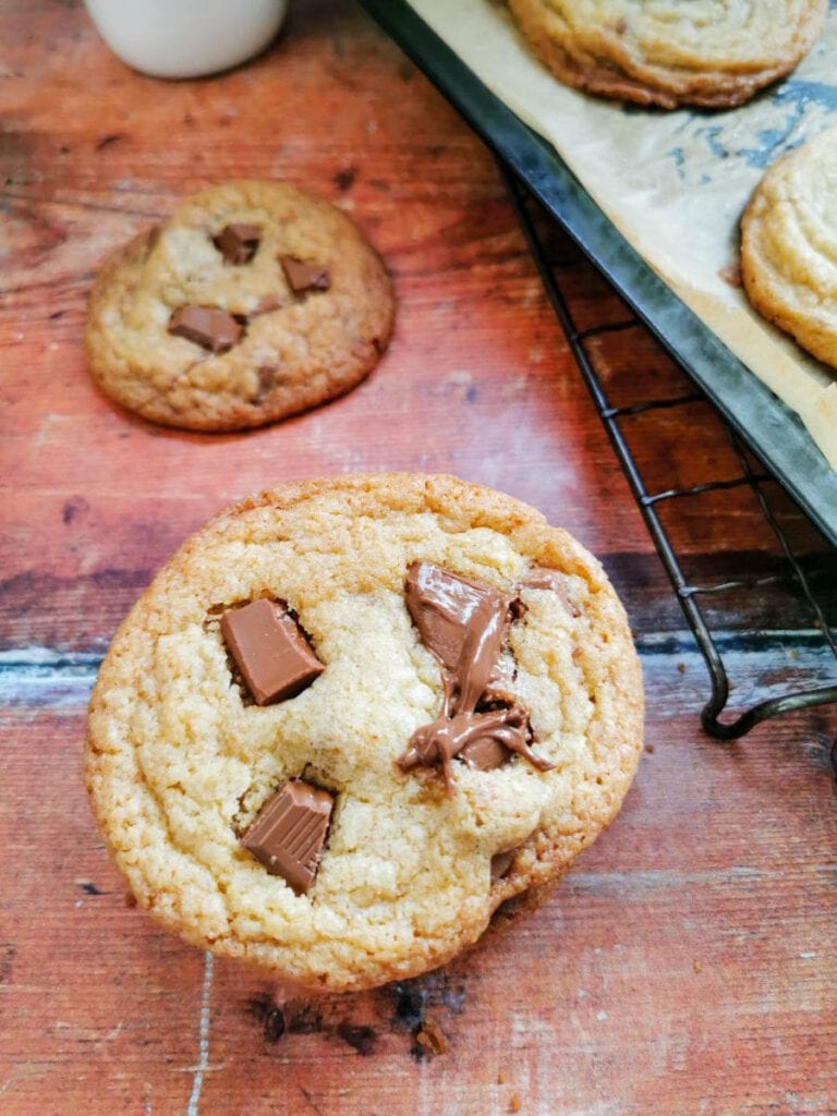 An ariel view of a stack of cookies with chocolate chips. A bottle of milk and a tray of cookies are in the background