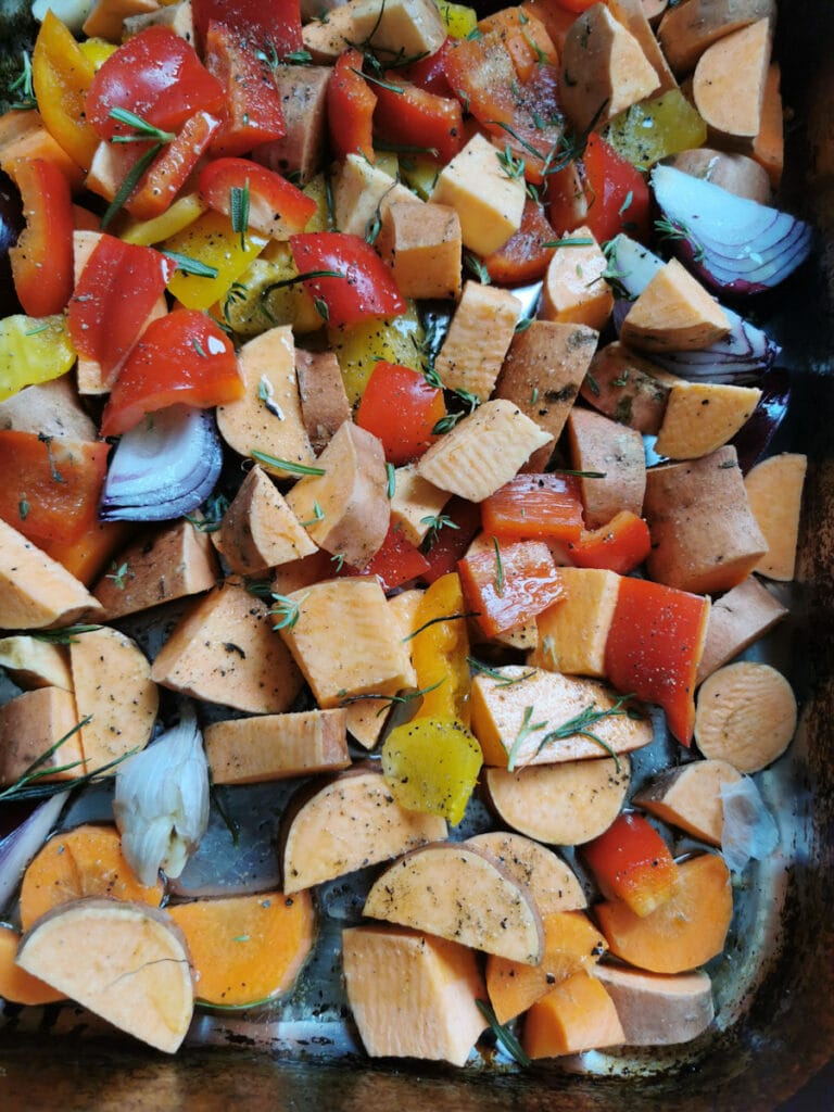 chopped sweet poatoes, onion, red peppers, garlic and herbs in a silver roasting tin.