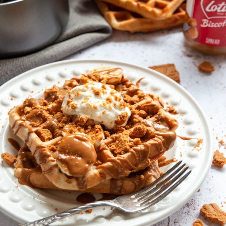 two waffles on a white plate with sliced bananas, melted Biscoff spread and whipped cream.