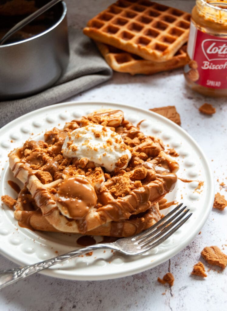 two waffles on a white plate with sliced bananas, melted Biscoff spread and whipped cream.