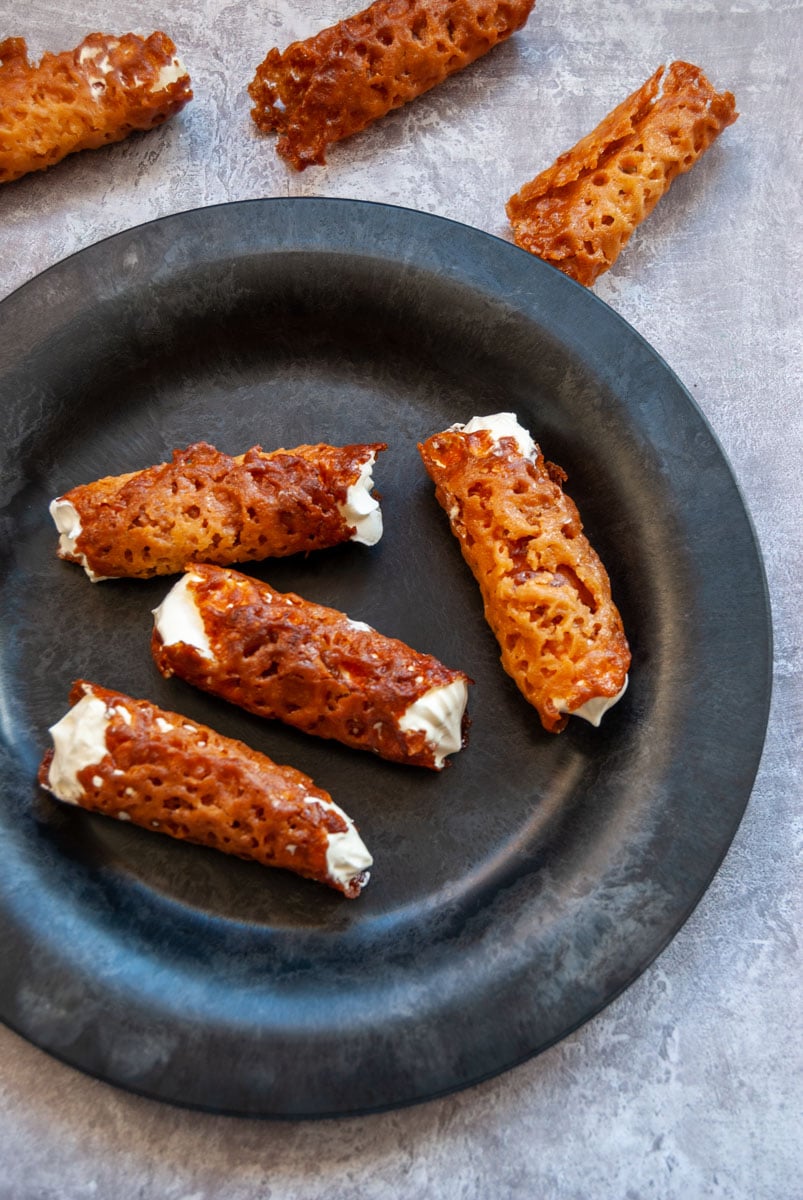 a black plate with four brandy snap cookies filled with whipped cream.