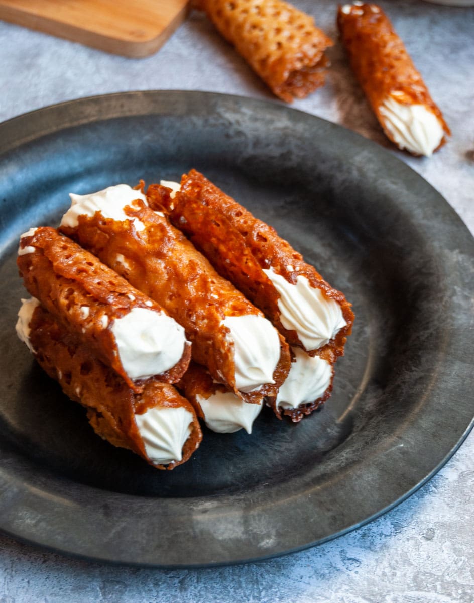 a black and grey plate of brandy snap cookies filled with whipped cream.