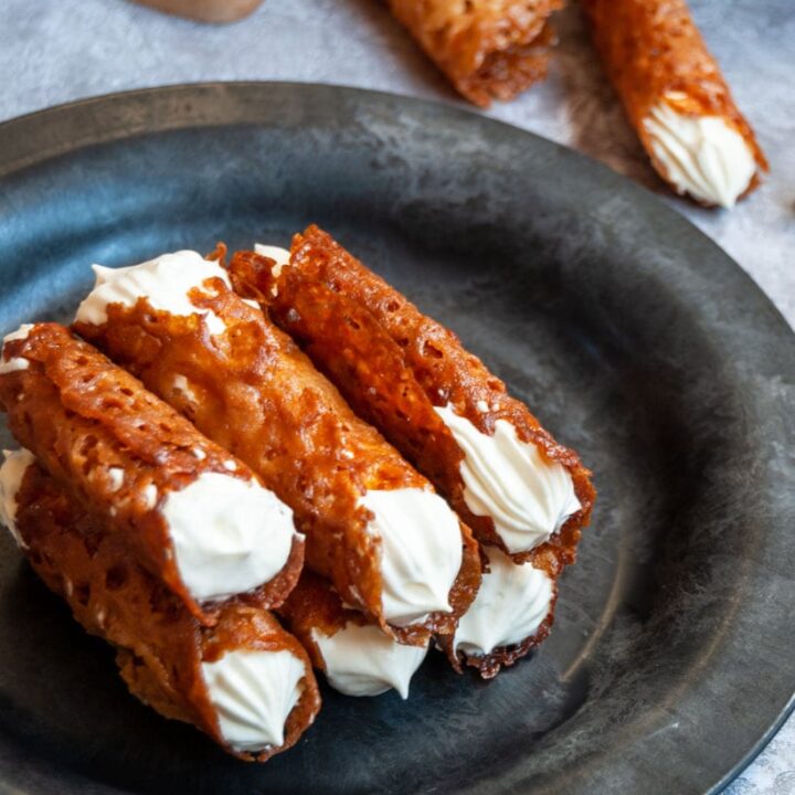 a black and grey plate of brandy snap cookies filled with whipped cream.