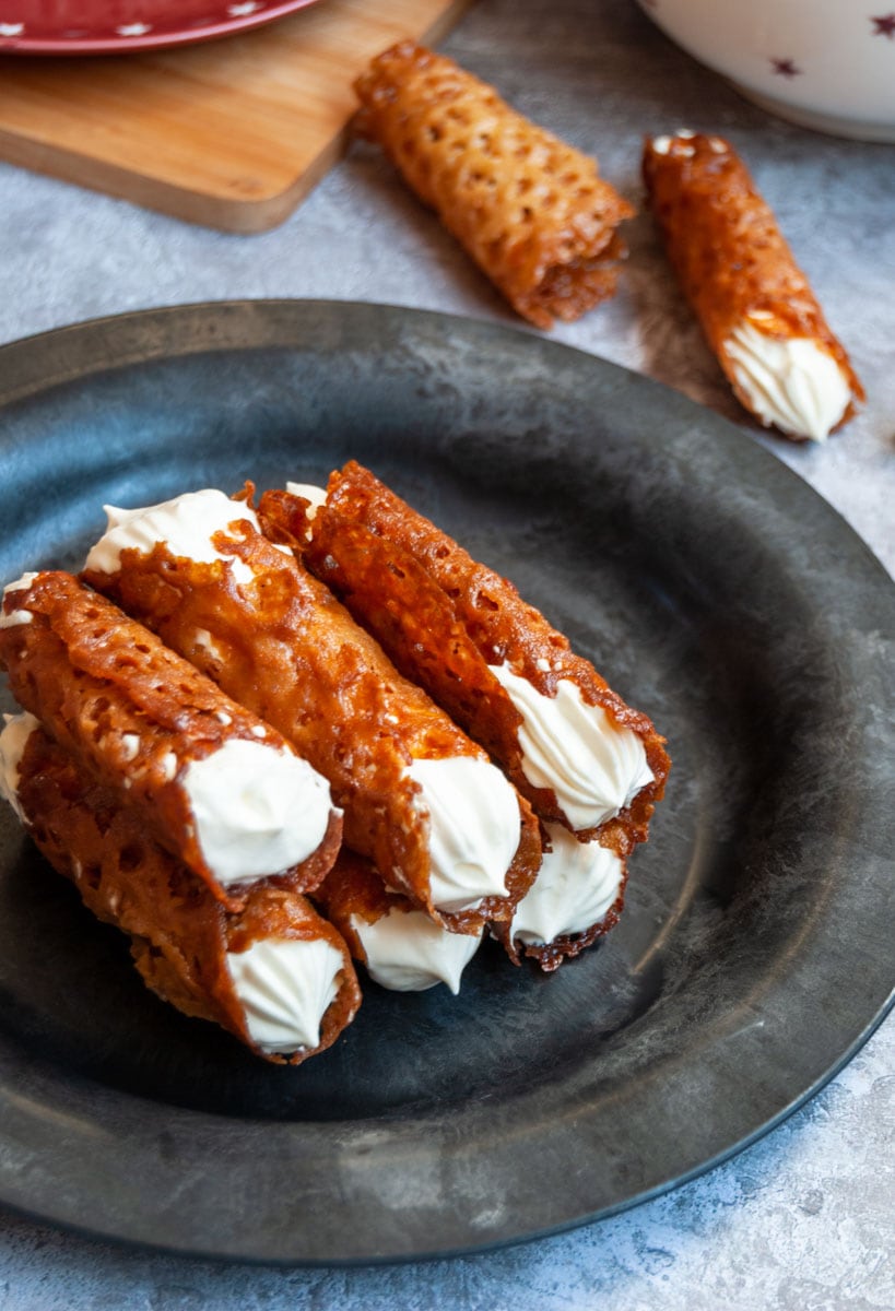 a black and grey plate of brandy snap cookies filled with whipped cream.