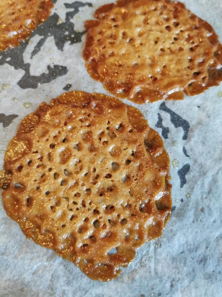 two freshly baked brandy snap cookies on a lined baking tray.