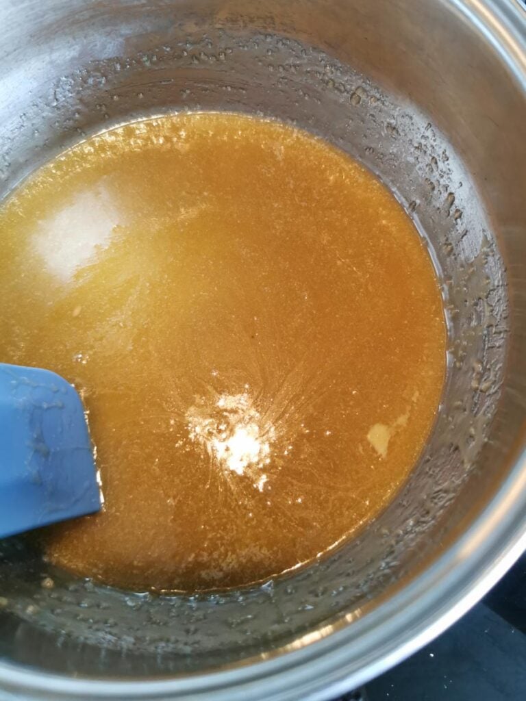 melted brown sugar, butter and golden syrup in a saucepan with a blue spatula.