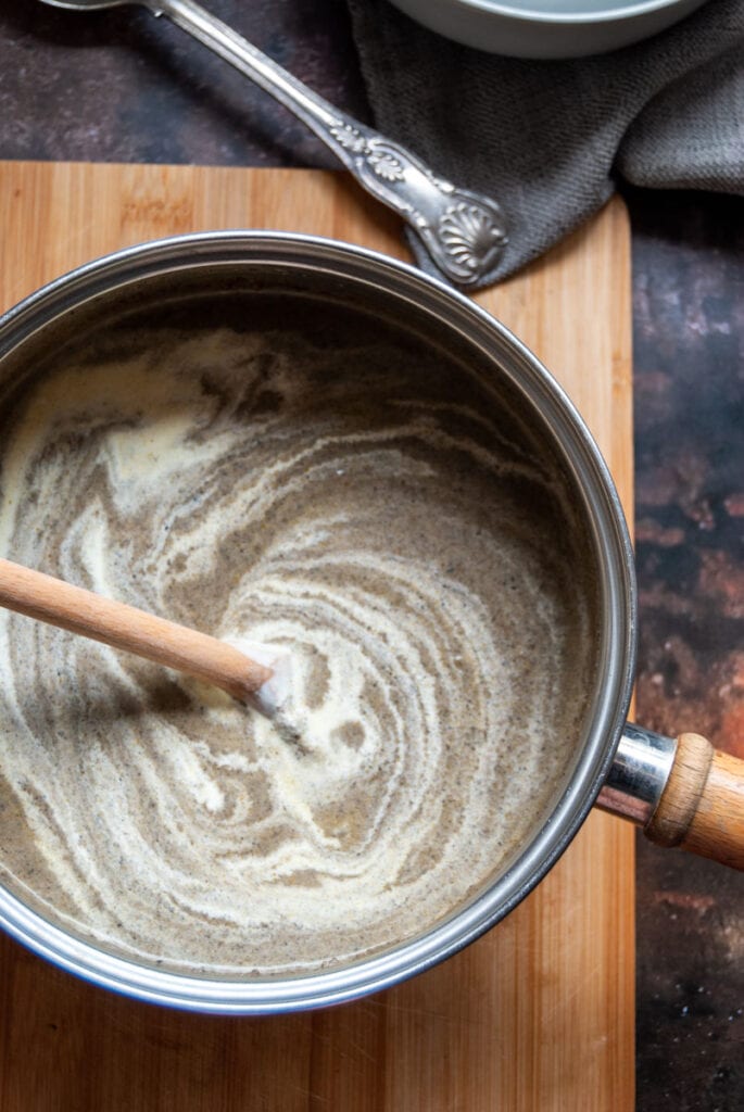 a pan of mushroom soup with cream and a wooden spoon.