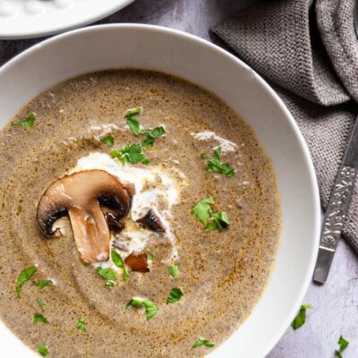 a white bowl of mushroom soup with a swirl of cream and chopped parsley.