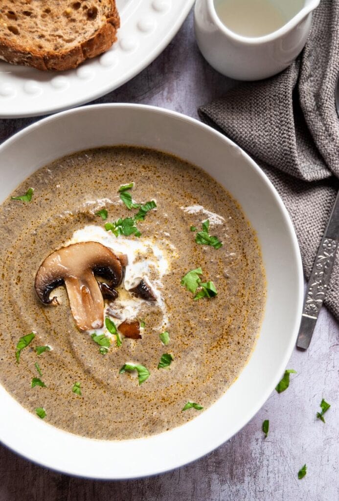 a white bowl of mushroom soup with a swirl of cream and chopped parsley.