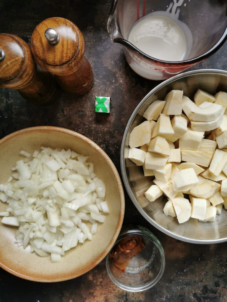 bowls of chopped onion, chopped parsnips, curry paste, a jug of cream, a stock cube and a wooden salt and pepper mill