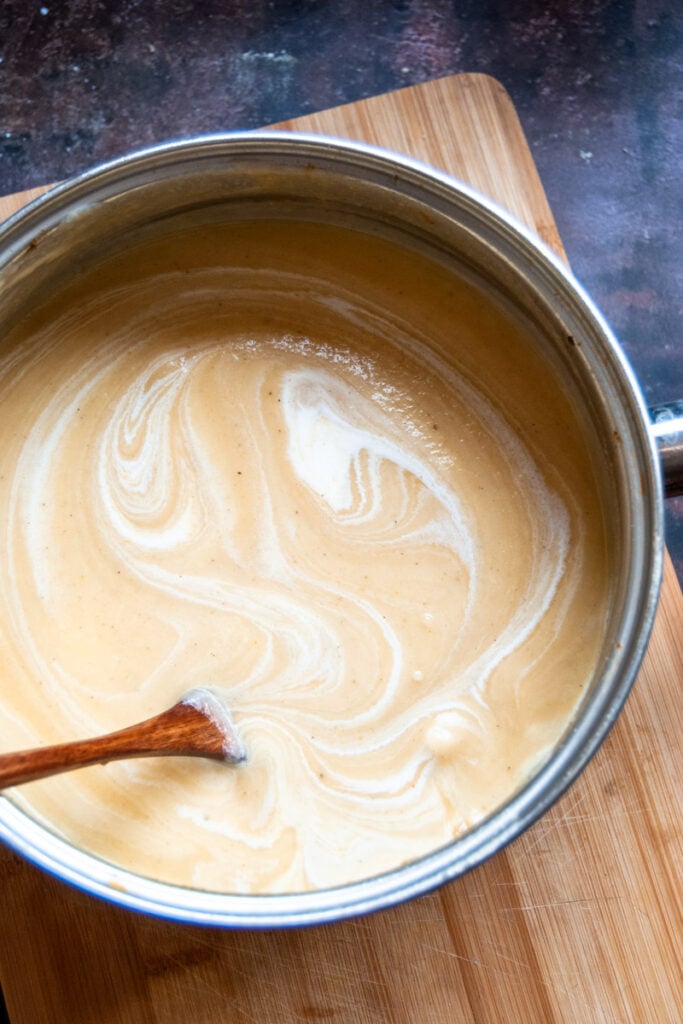 a large pan of parsnip soup with cream and a wooden spoon.